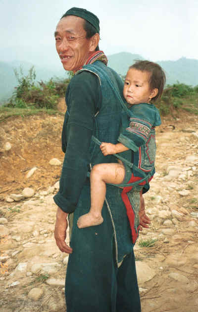 Black Hmong man carrying his granddaughter on his back in a baby carrier in the hills around Sa pa, Northern Vietnam 9510i28.jpg